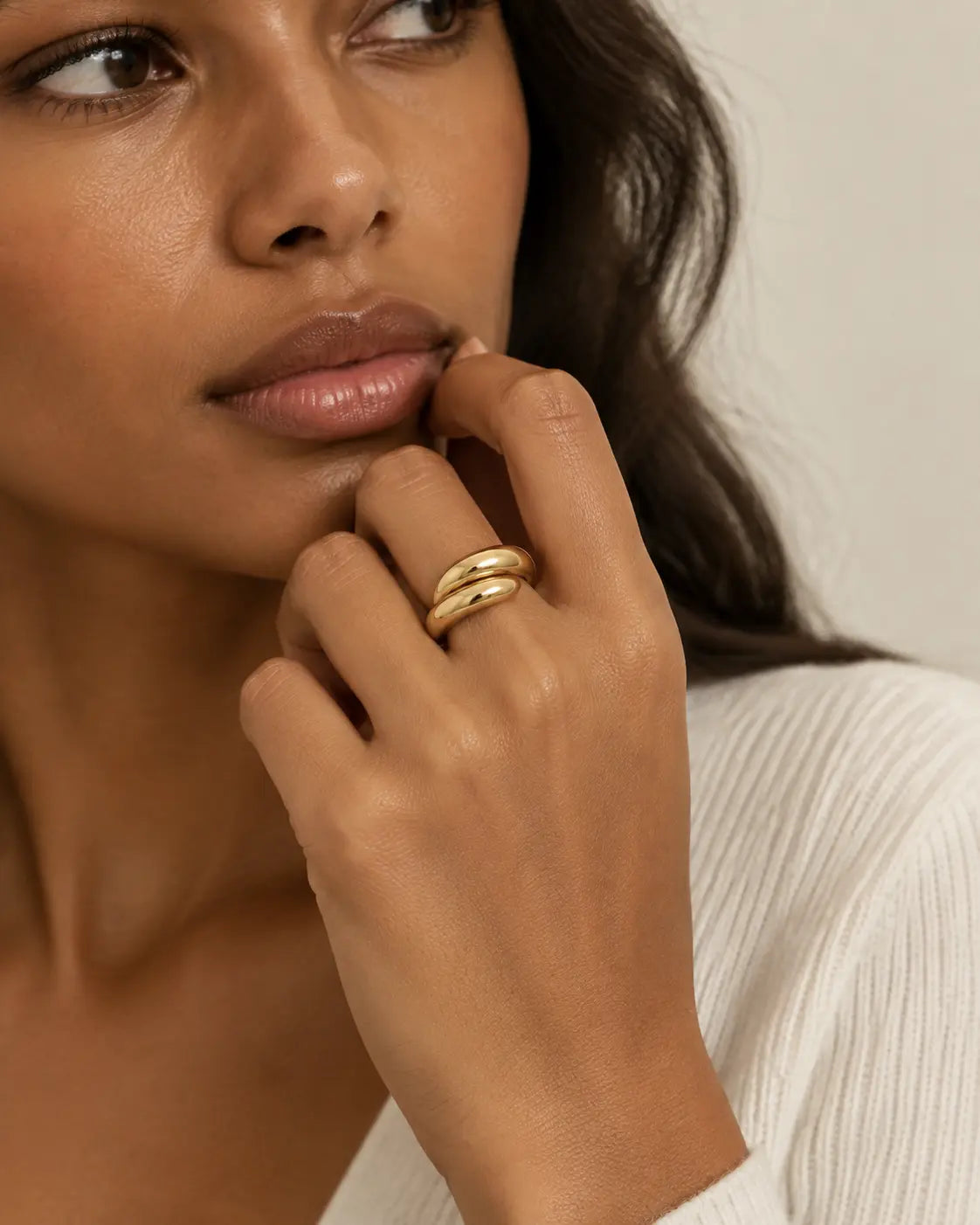 Gold-tone ring with two rounded contours, worn on a hand beside the lips.