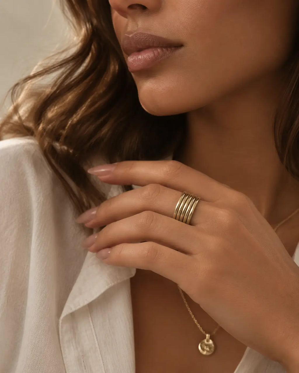 Gold-tone open band ring with multiple parallel rails, worn on a hand beside an open white collar.