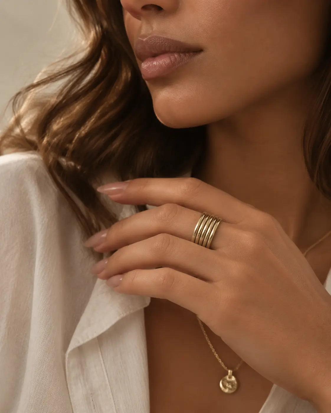 Gold-tone open band ring with multiple parallel rails, worn on a hand beside an open white collar.