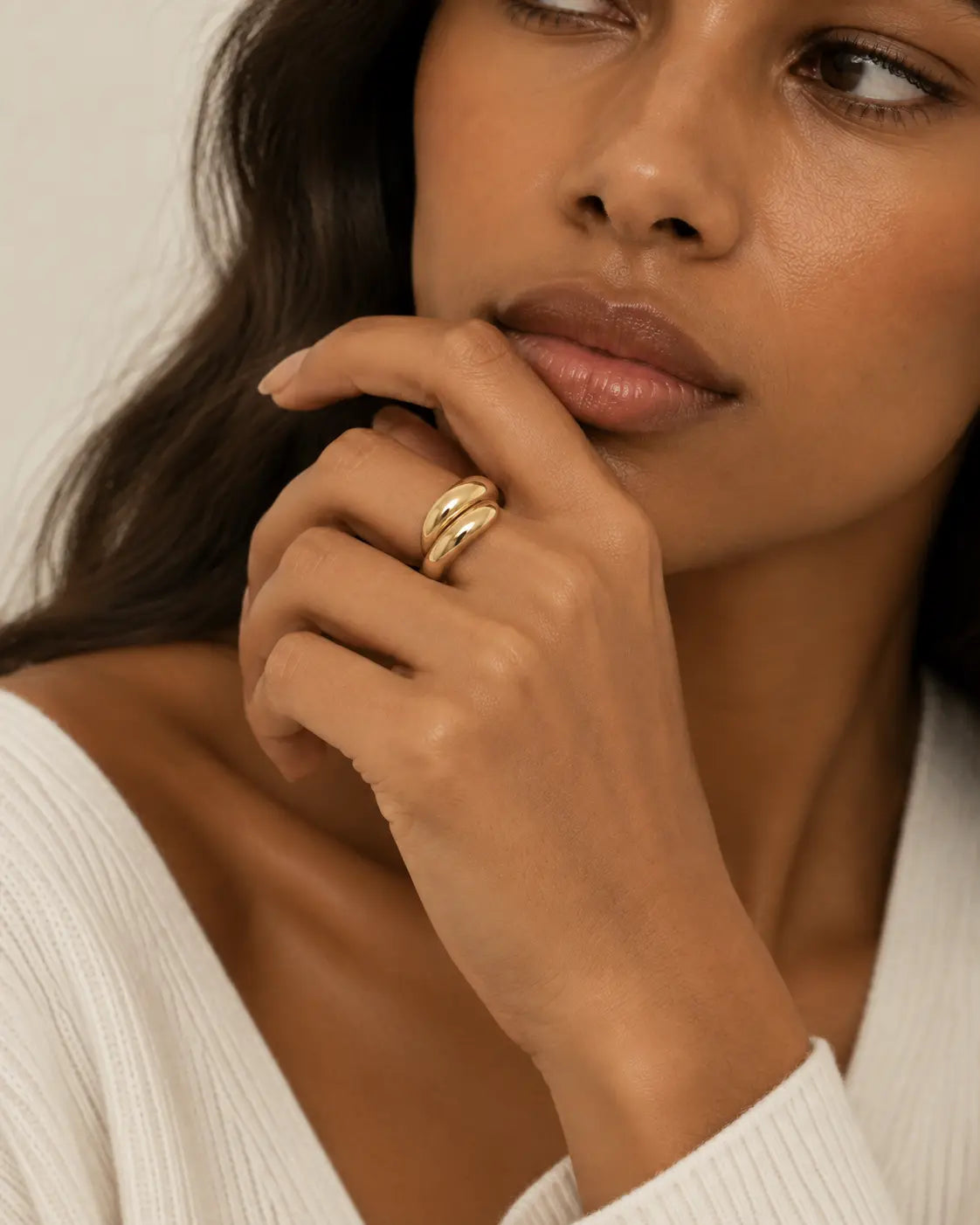 Gold-tone ring with two rounded contours, worn on a hand near the chin.