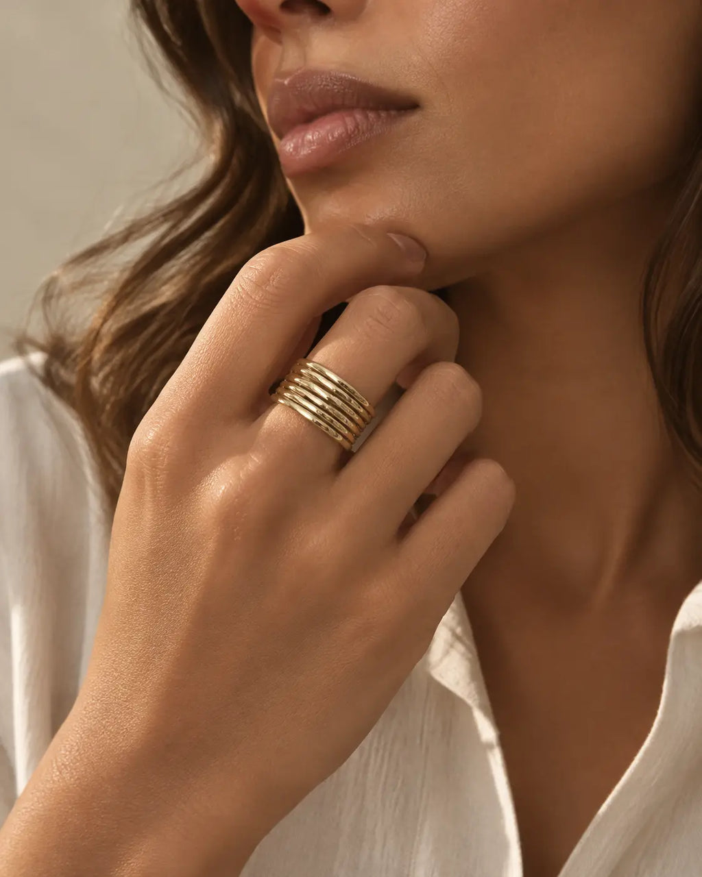 Gold-tone open band ring with multiple parallel rails, worn on a hand near the chin.