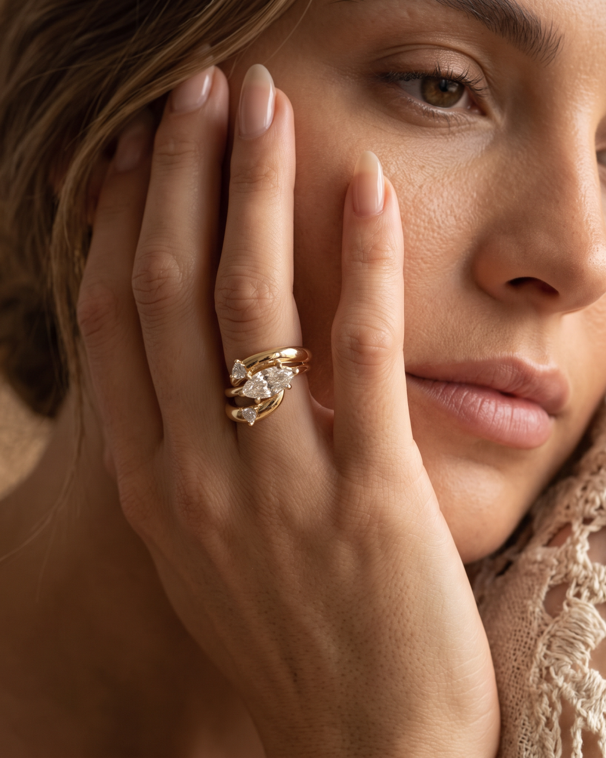 Gold-tone open wrap ring with stone accents at both ends, worn on a hand beside the face.