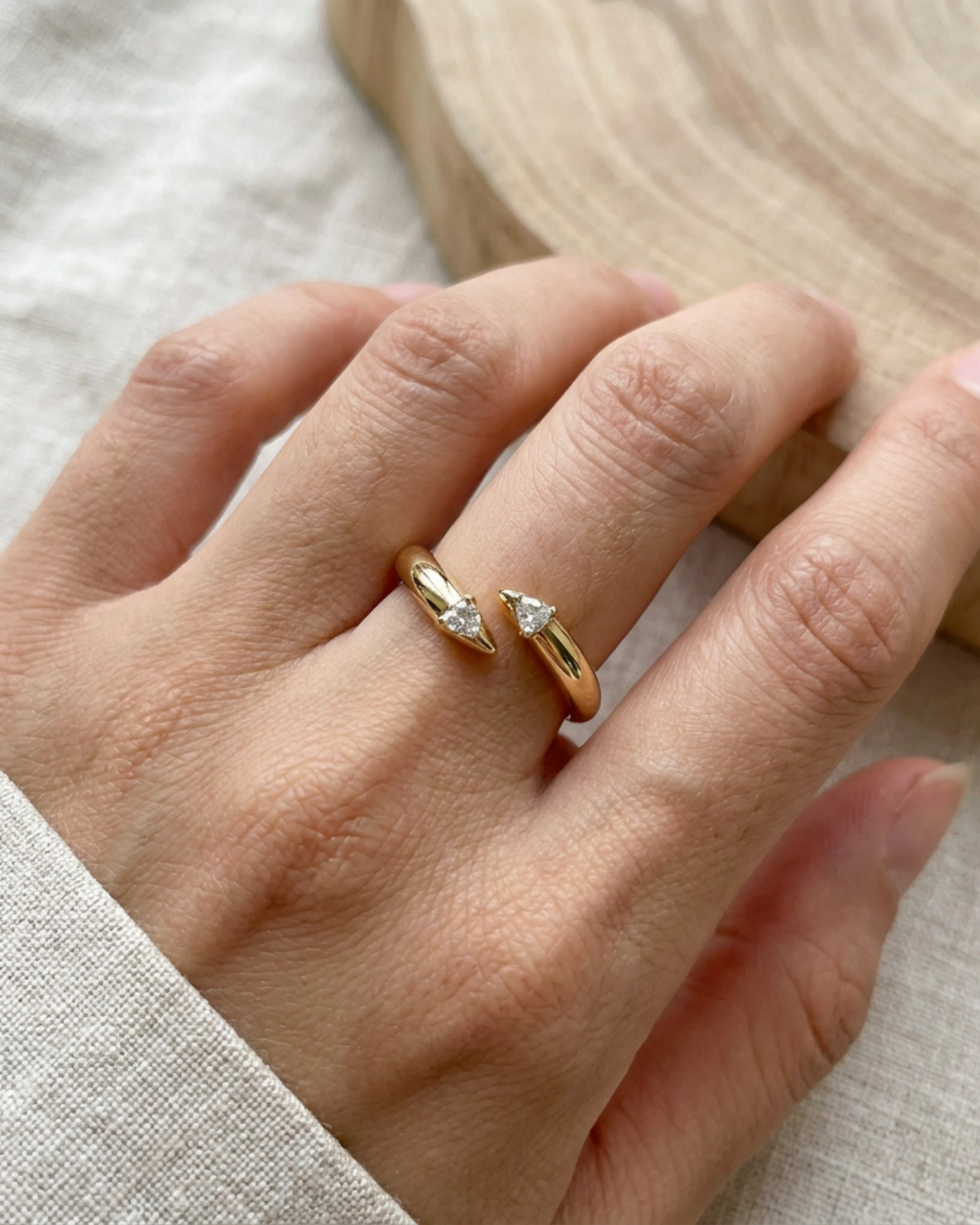 Gold-tone open wrap ring with stone accents at both ends, worn on a hand resting on light fabric.