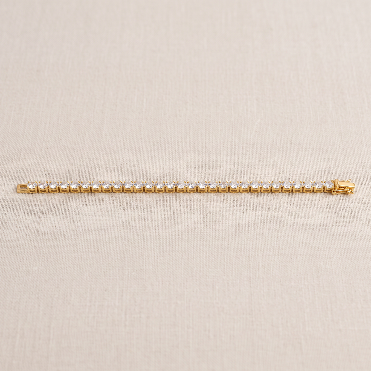 Gold-tone tennis bracelet laid flat, showing a row of round clear stones and an open clasp.