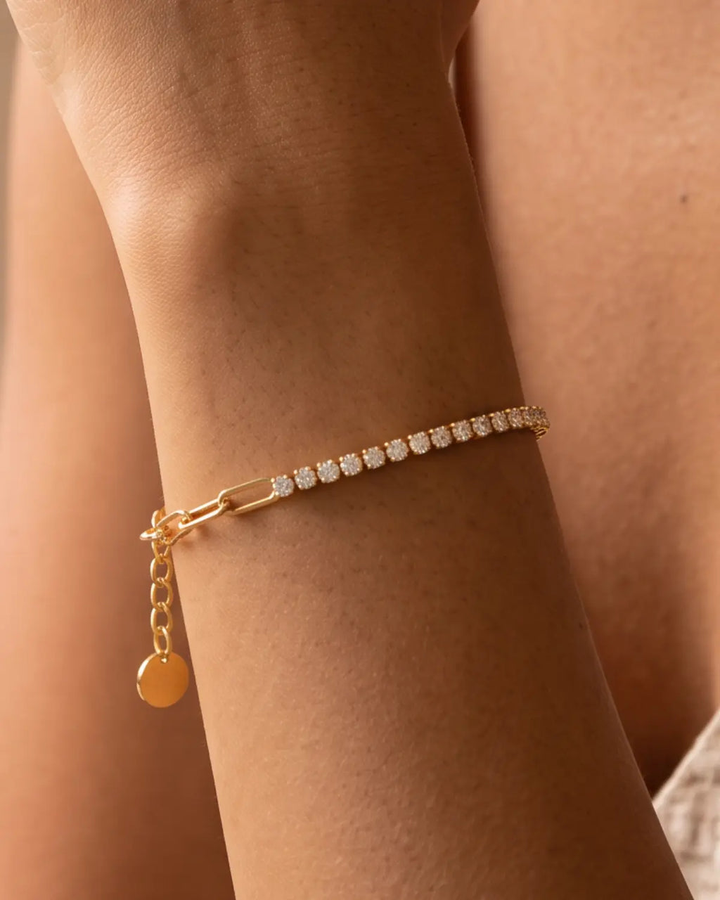 Gold-tone bracelet combining paperclip links and a row of clear stone accents, worn with the stone row and extension chain visible.