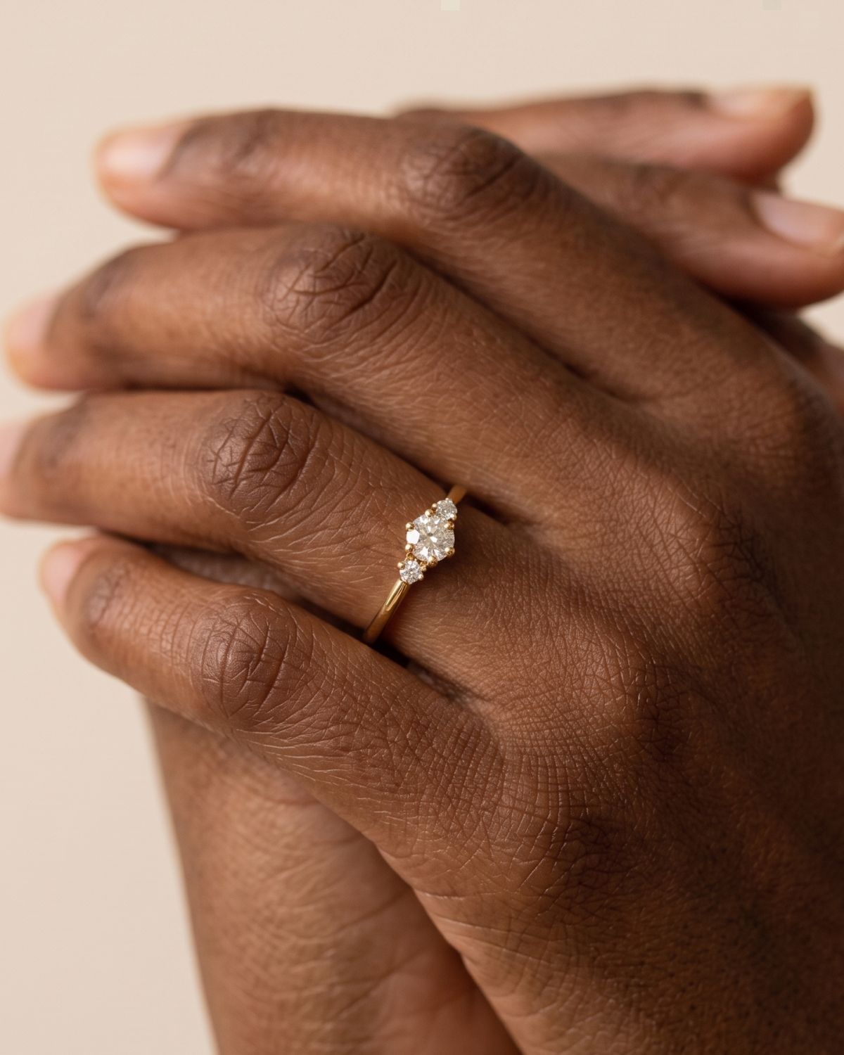 Gold-tone band ring with a central three-stone cluster, worn on gently clasped hands.