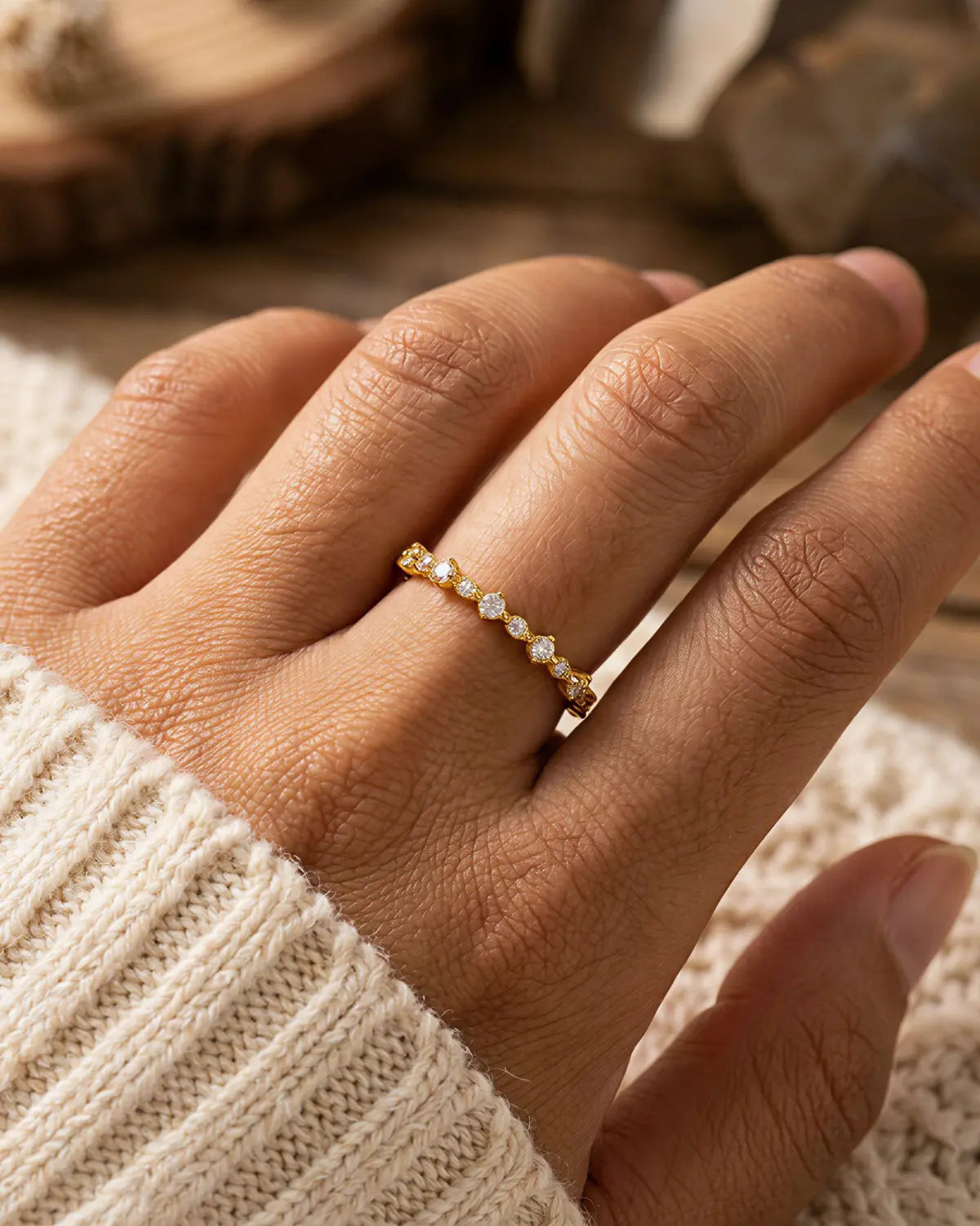 Gold-tone band ring with a row of clear stone accents, worn on a hand beside cream knitwear.