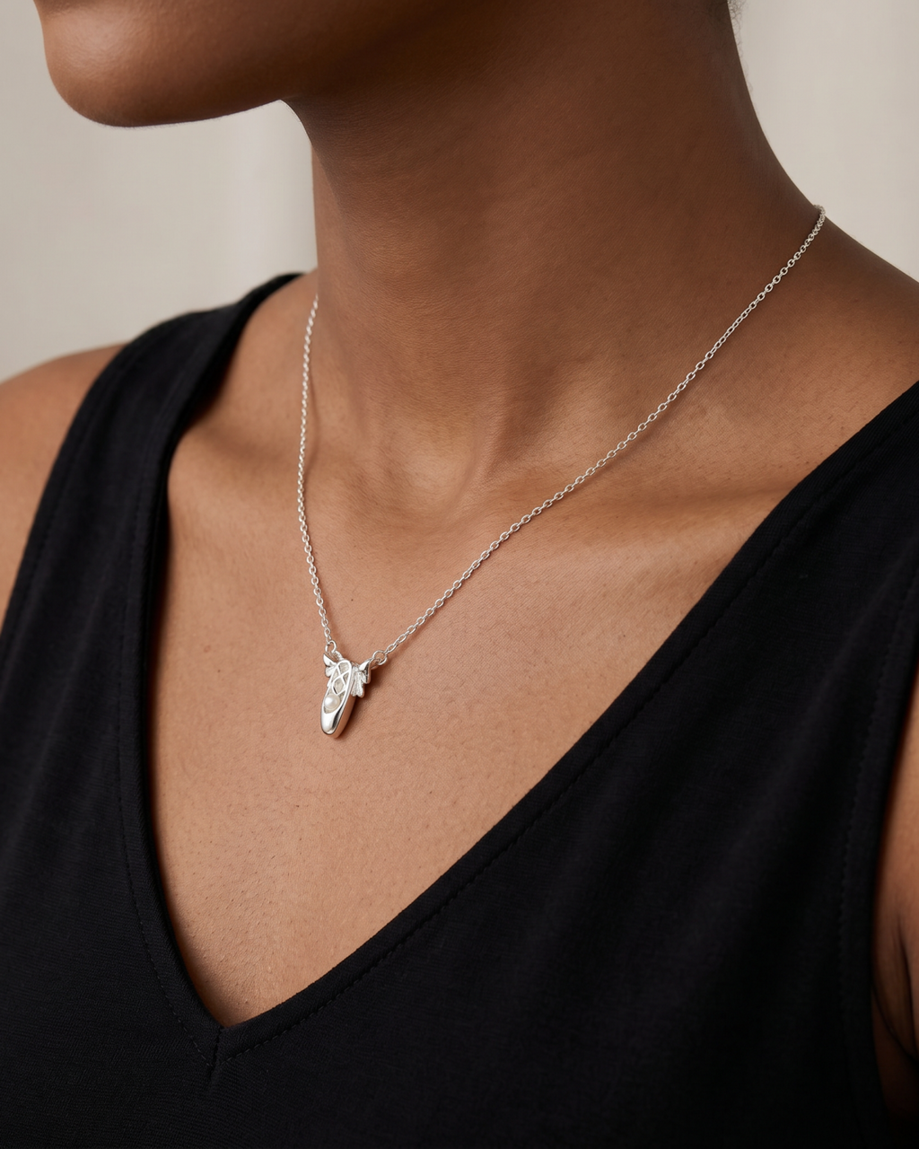 Silver-tone necklace with two ballet-slipper pendants, wider view of the necklace at a black neckline.